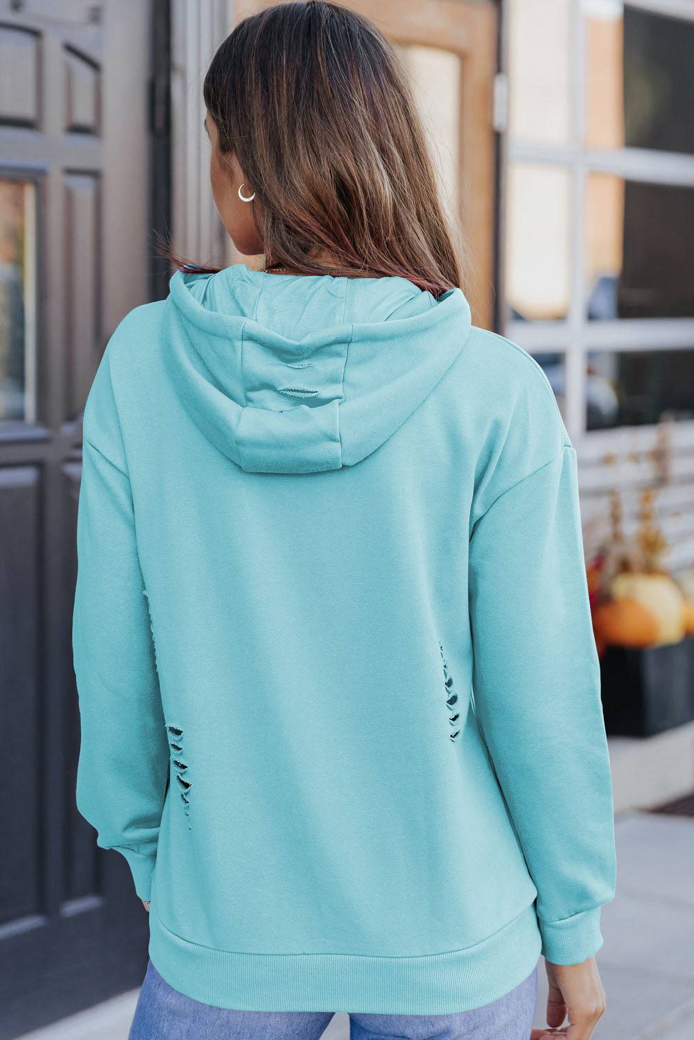 a woman wearing a light blue hoodie and ripped jeans