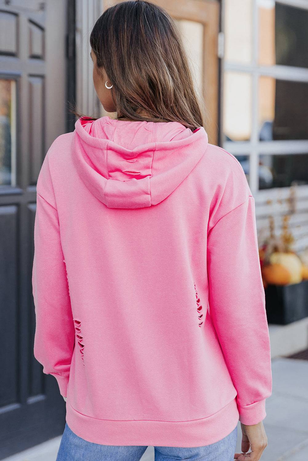 a woman wearing a pink hoodie and ripped jeans